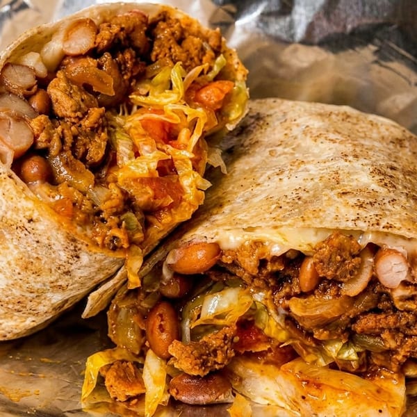 Two halves of a large, grilled burrito filled with meat, beans, and vegetables on foil.